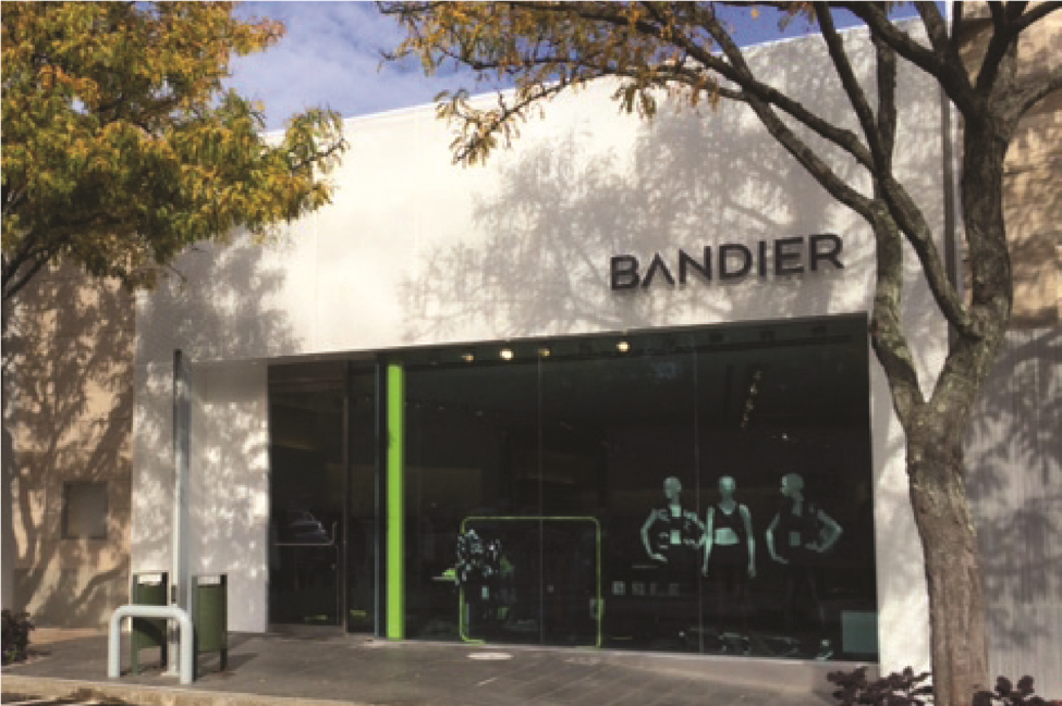 A street-level architectural view of the Bandier luxury activewear boutique storefront in Soho, built by MOMA Construction Group, featuring a clean white building facade, expansive glass windows, and minimalist black branding signage.