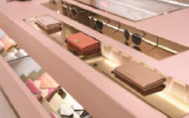 A high-end luxury retail display interior built by MOMA Construction Group for the Chloé boutique, featuring custom blush pink tiered shelving, integrated warm LED accent lighting, and elegant glass cases showcasing designer leather handbags and accessories.