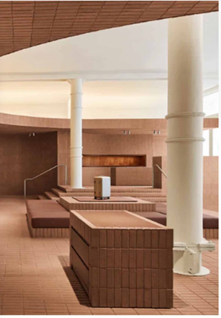 A multi-level retail showroom interior in Soho featuring terracotta brick tile steps and custom display platforms with large structural white columns and a travel suitcase on display.