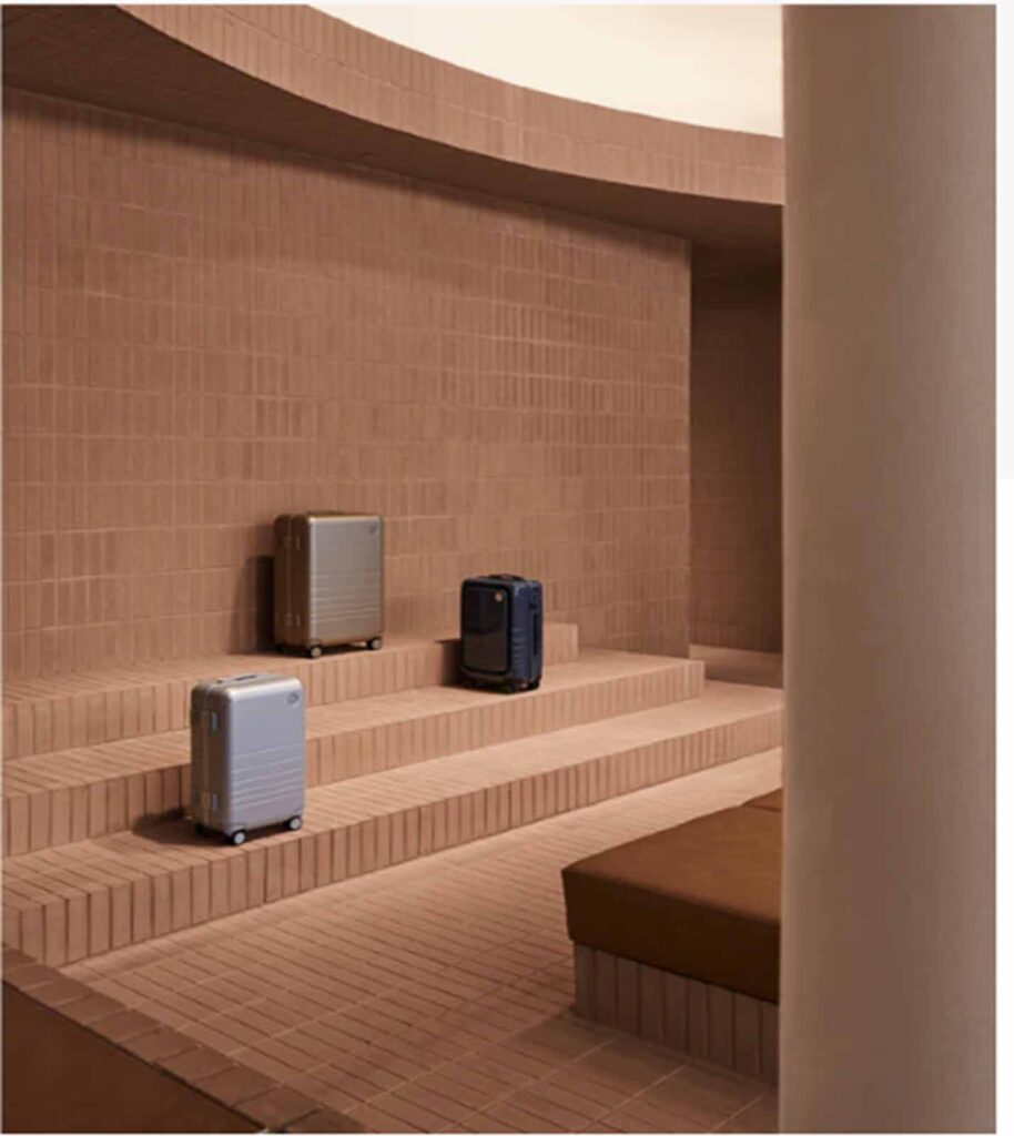 A modern, multi-level retail showroom interior in Soho featuring built-in terracotta-tiled bench seating and stepped platforms used to display luxury travel luggage cases.