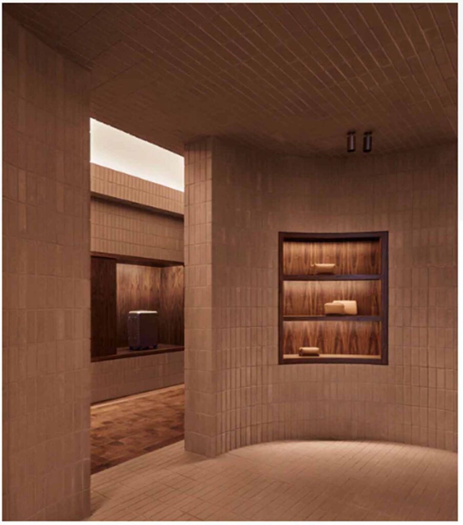 A modern commercial showroom interior in Soho featuring a curved terracotta brick-tiled wall with an illuminated, built-in dark wood display shelving unit.