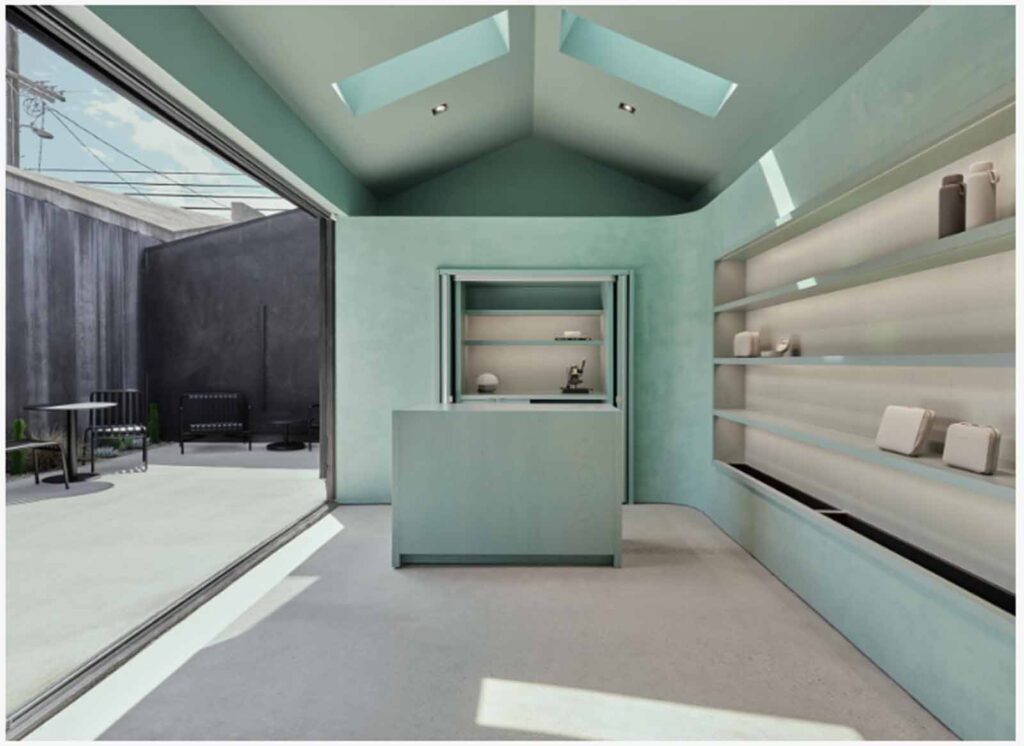 A modern, light teal boutique interior on Abbot Kinney featuring pitched ceilings with twin skylights, sleek built-in shelving, and a central checkout counter looking out to an open-air concrete patio.