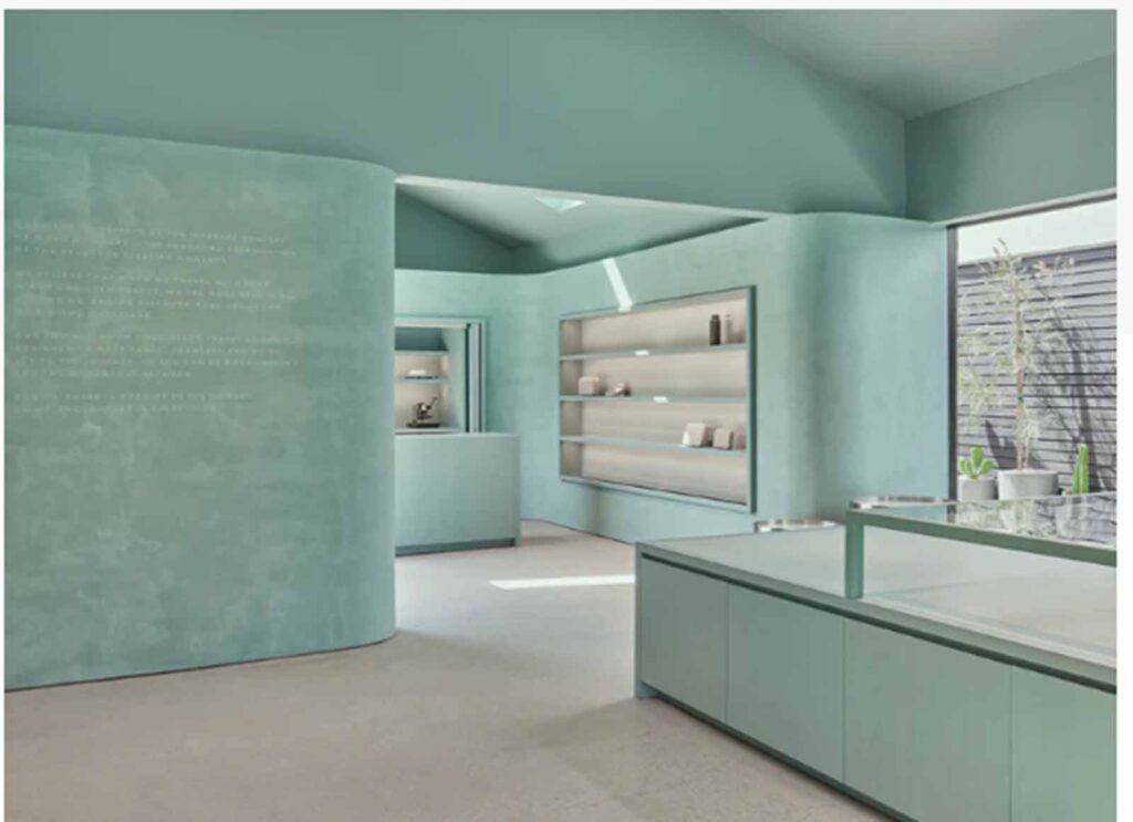 A wide interior view of the Monos showroom on Abbot Kinney featuring mint green walls and built-in shelving, with a minimalist checkout counter in the foreground and a glass-block accent wall in the background.