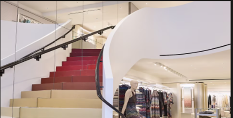 A modern curved white staircase with red carpet inside the Missoni Madison Avenue showroom, overlooking retail clothing displays.
