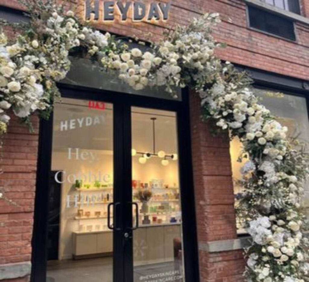Commercial retail storefront renovation on 19th Street by MOMA Construction Group showcasing a historic red brick facade with a black-framed glass entrance door decorated with a large white floral archway for Heyday