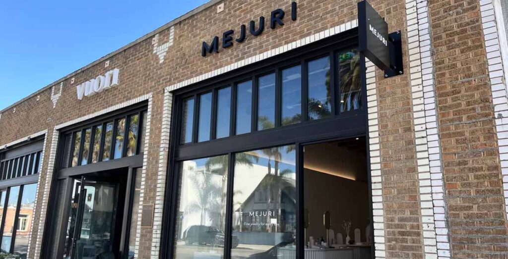 Commercial retail boutique exterior storefront renovation by MOMA Construction Group featuring a historic brick facade, symmetrical double-door entrance, and clean MEJURI brand sign bands under a blue sky.