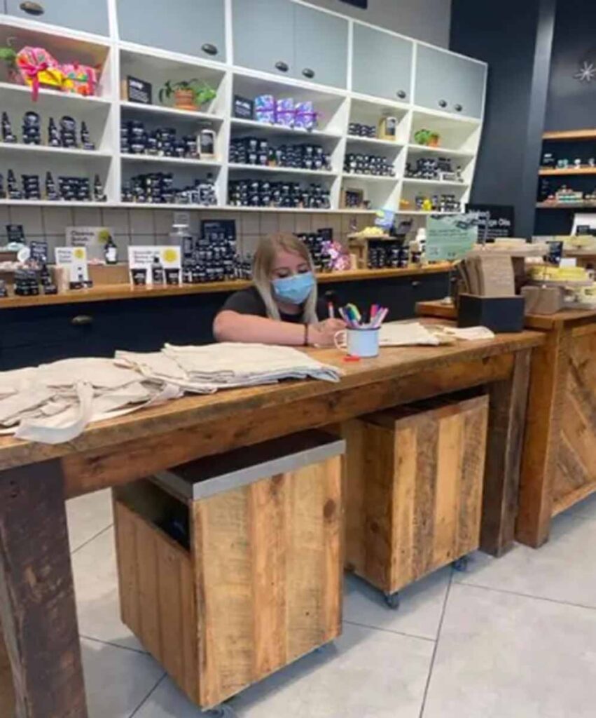 Commercial retail interior fit-out by MOMA Construction Group featuring a custom rustic timber checkout counter with mobile under-counter storage cabinets and a retail employee reviewing documentation.