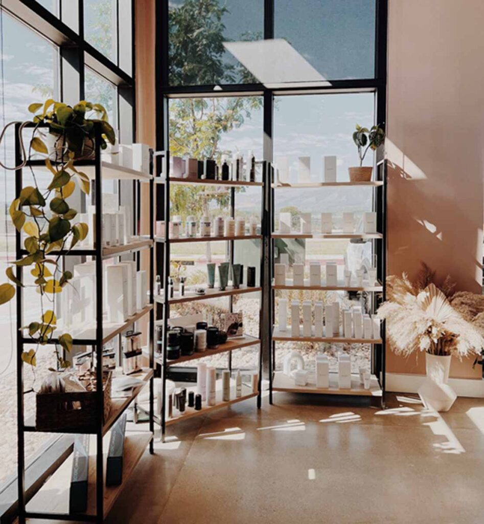 Modern commercial boutique interior construction featuring floor-to-ceiling black structural window framing, custom black steel grid display shelving units, and polished concrete flooring under natural light.