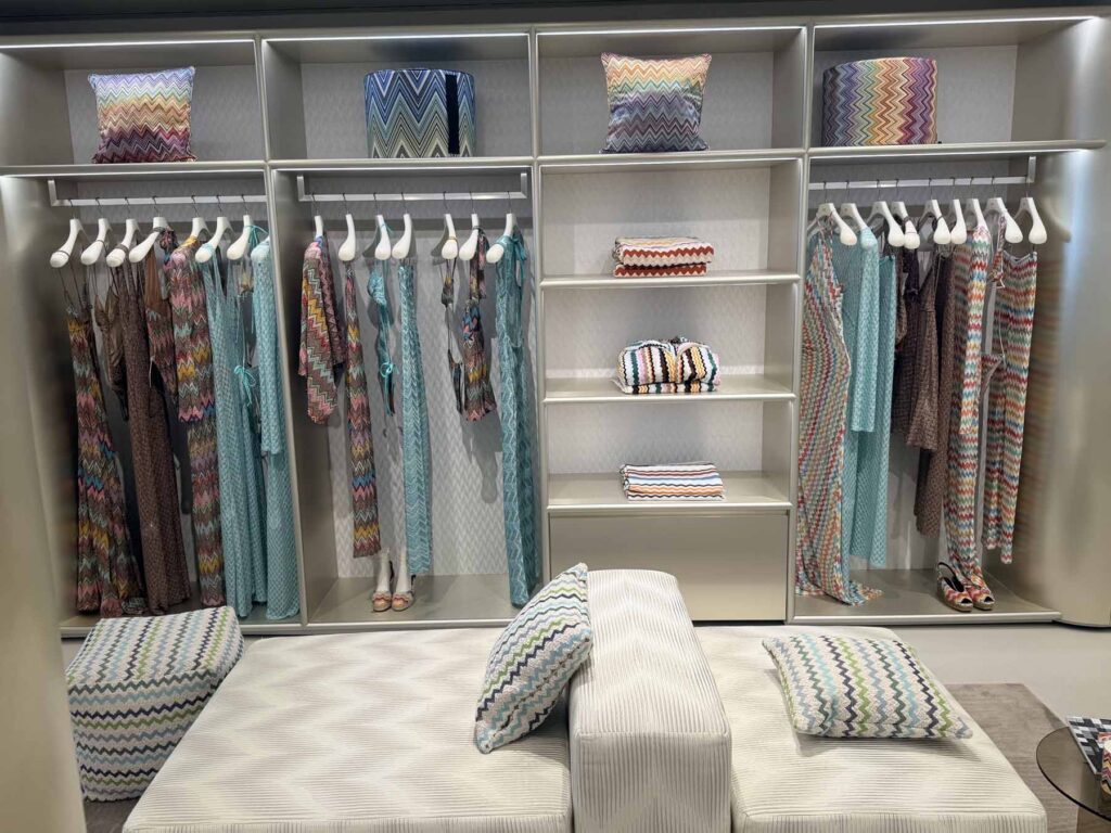 Modeern luxury walk-in closet and showroom display featuring organized designer apparel, custom shelving, and a patterned accent bench.