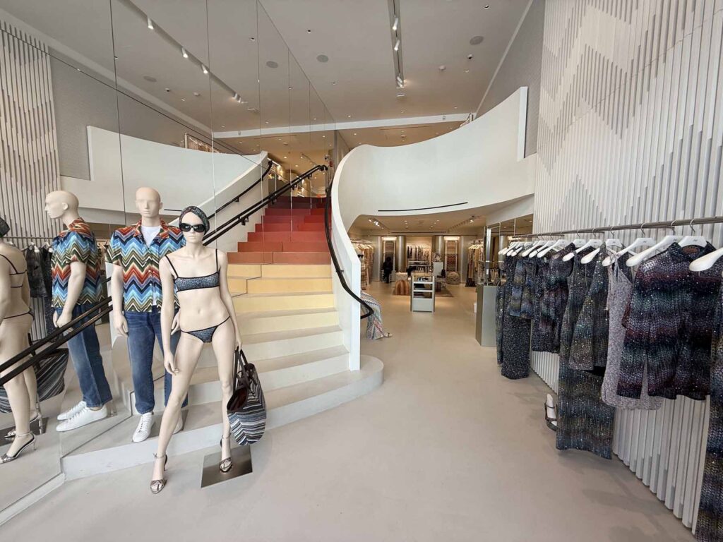 Modern Madison Ave fashion retail showroom featuring an elegant curved architectural staicase, custom mannequins, and minimalist apparel display racks.