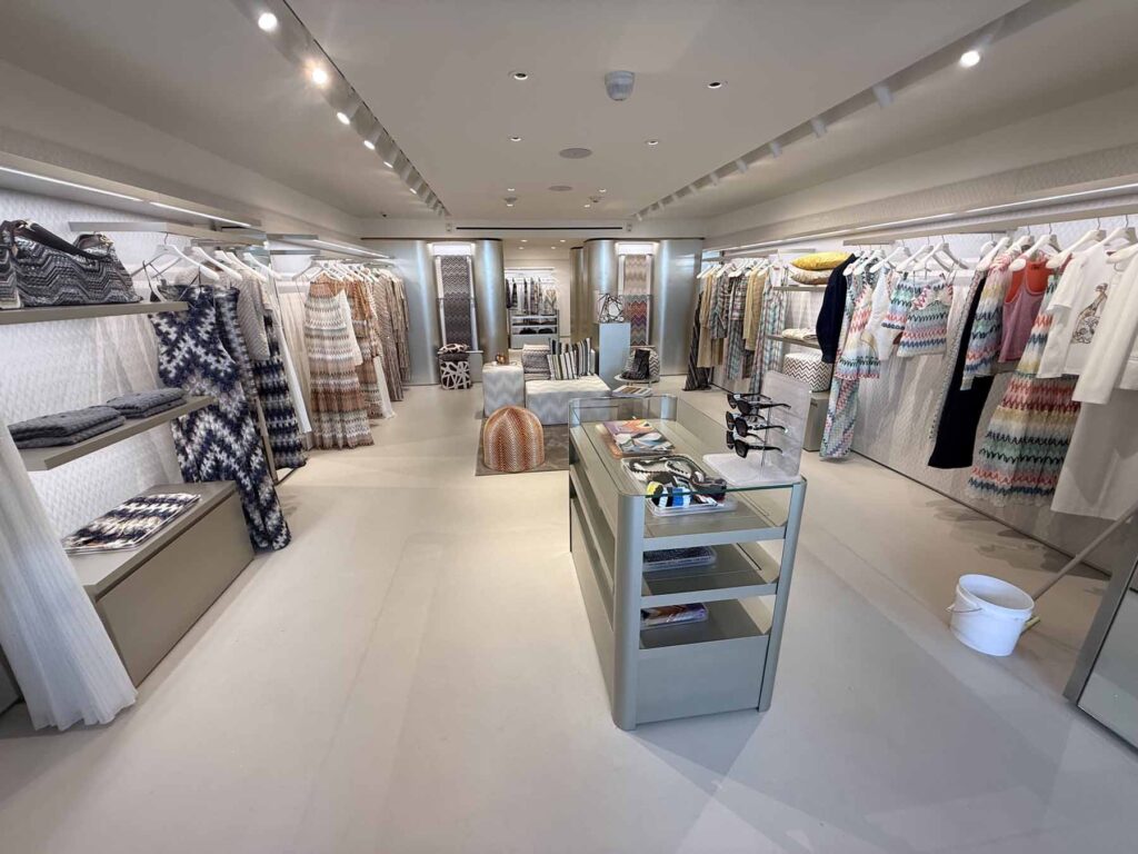 Interior design showroom on Madison Ave showcasing premium minimalist clothing displays, architectural recessed lighting, and a modern central glass display case.