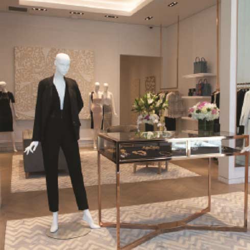 A polished interior view of the Kimora Lee Simmons luxury clothing boutique built by MOMA Construction Group, featuring an elegant fashion mannequin showcasing a sleek black designer suit next to a custom rose gold and glass display counter.
