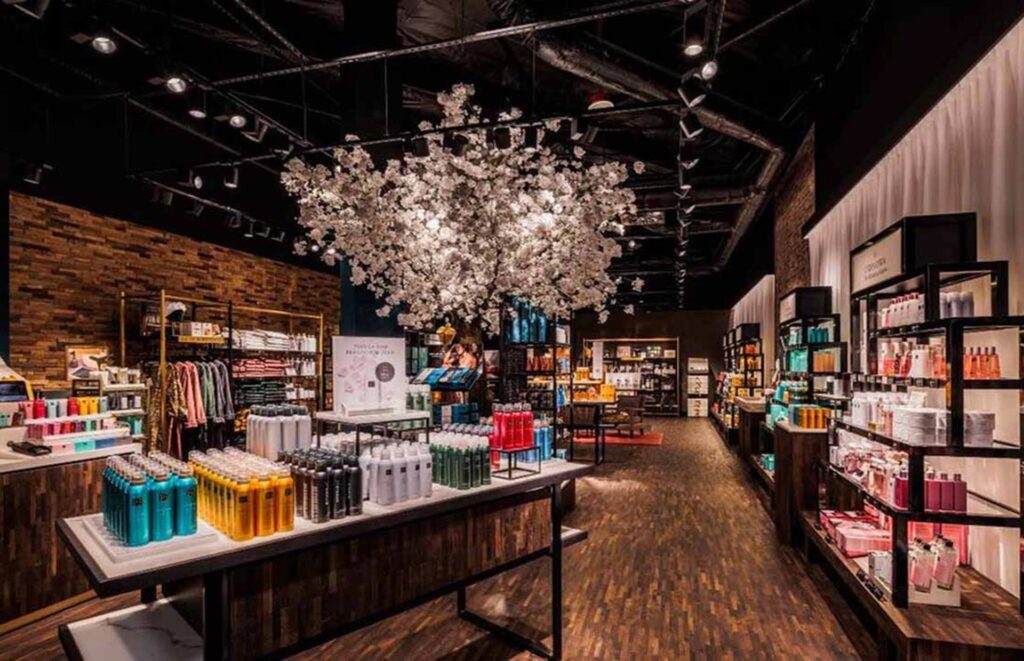 Modern premium retail boutique interior featuring on elegant white floral cherry blossom centerpiece, built-in display shelving with curated products, dark wood flooring, and industrial track lighting.