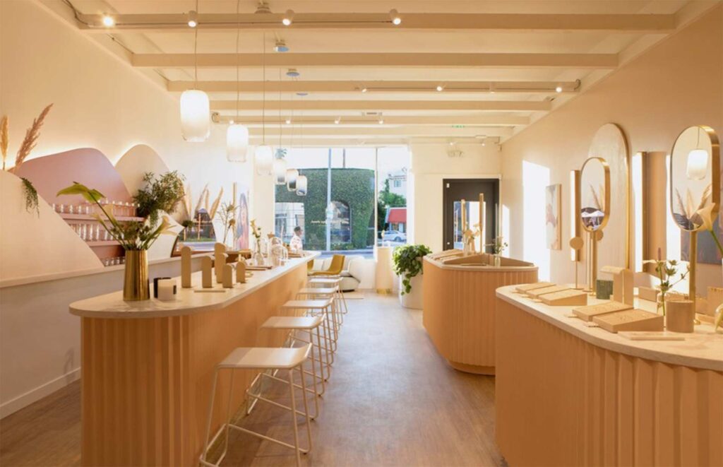 Modern premium skincare boutique and beauty showroom interior featuring a long curved light-wood service counter, minimalist bar stools, custom arched mirrors, and warm geometric lighting.