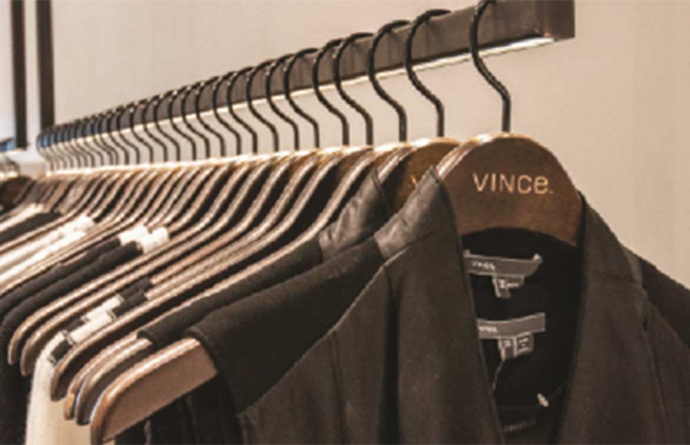 An interior view of a luxury clothing rack built by MOMA Construction Group for the Vince showroom, featuring dark designer jackets neatly arranged on custom branded wooden hangers.